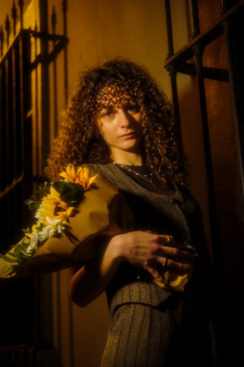 Free A woman with curly hair holds a sunflower bouquet against a dimly lit urban wall. Stock Photo