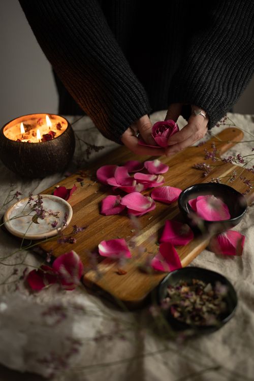 Free Hands arranging pink rose petals on a wooden board with a cozy candlelit ambiance. Stock Photo
