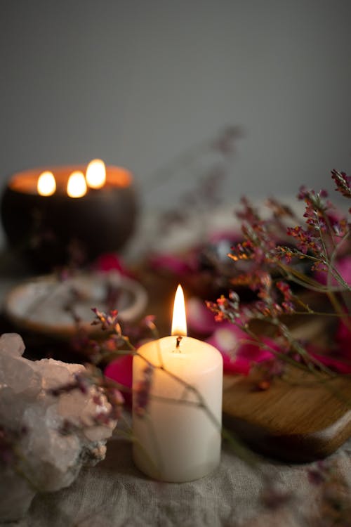 Burning Candle Next to Flowers and Wooden Board