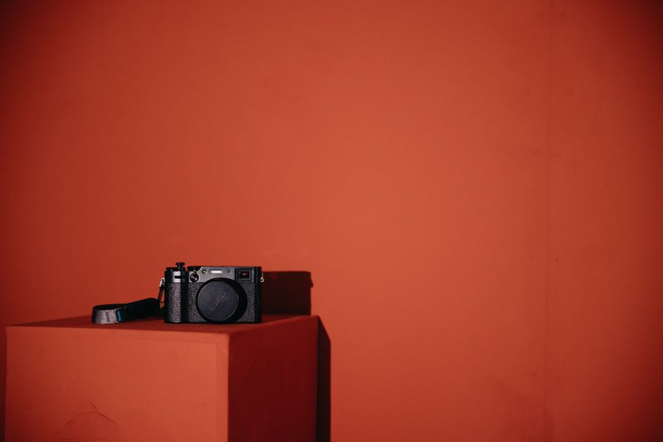 A sleek modern camera resting on a red display stand against a red backdrop, ideal for tech themes.