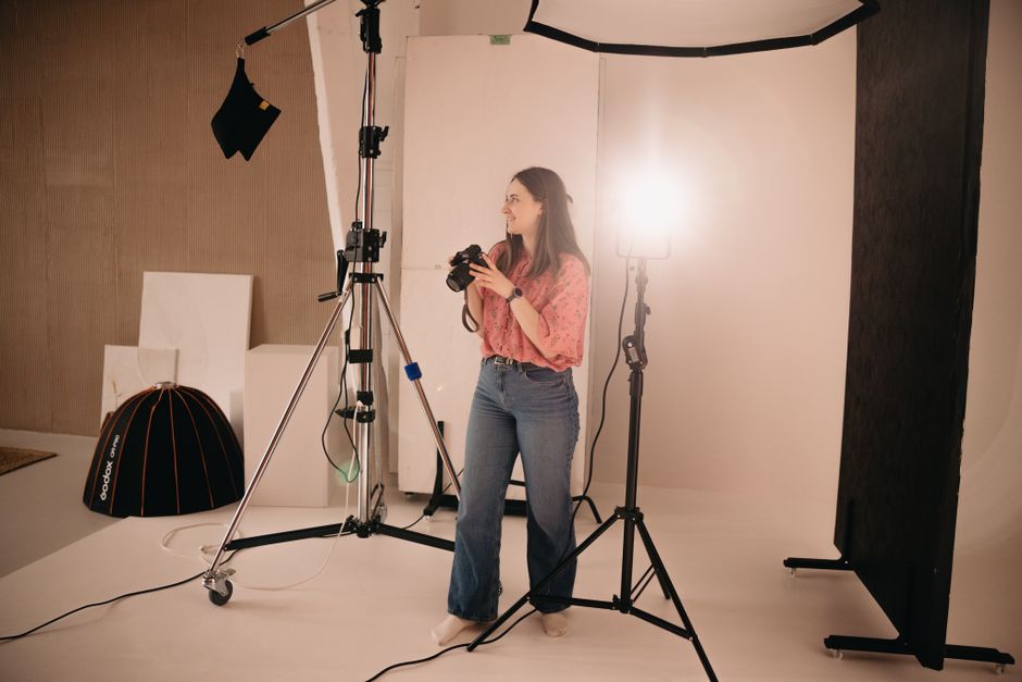 A woman holding a camera during a photoshoot in a well-equipped photo studio.