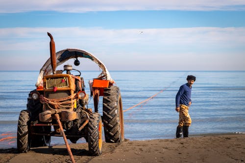 A man is standing next to a tractor on the beach