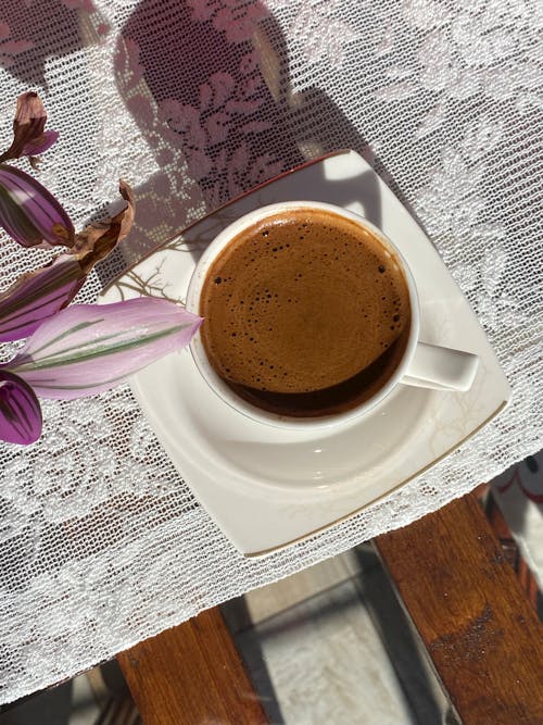 A cup of coffee on a table with a flower