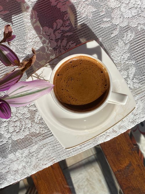 Free Top view of a cup of coffee on a lace tablecloth with floral decor in sunlight. Stock Photo