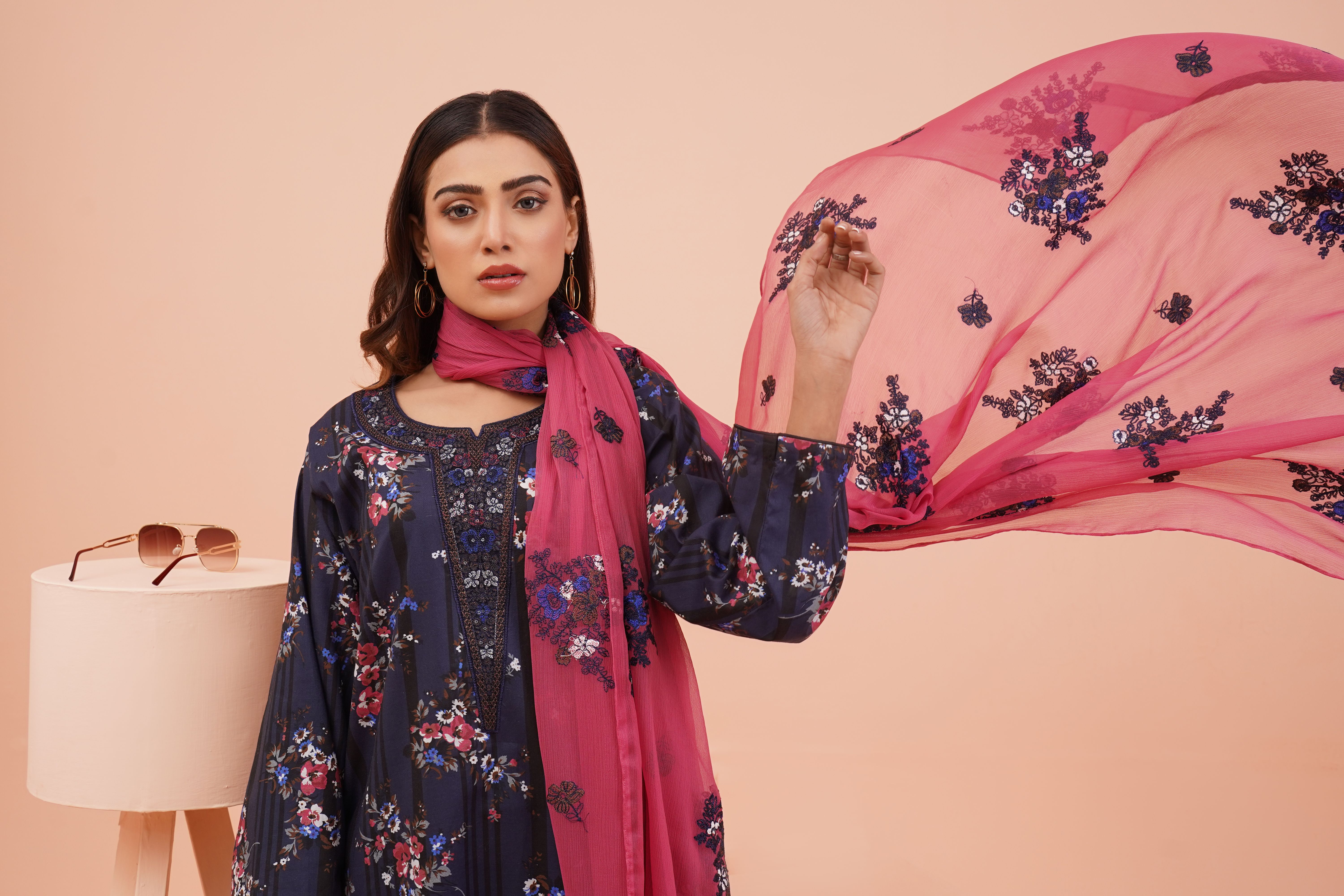 Portrait of a woman in traditional Pakistani attire holding a shawl in a studio setting.