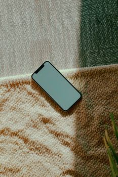A smartphone rests on a textured carpet, bathed in natural sunlight, offering a warm and relaxed feel.