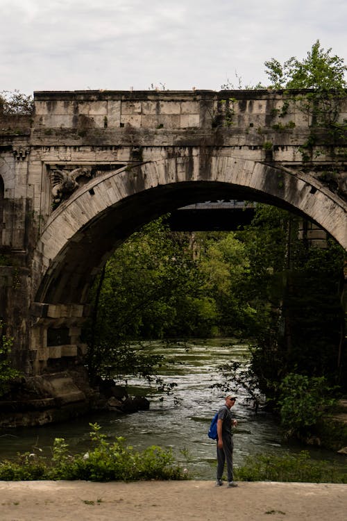 A man is standing under an old bridge