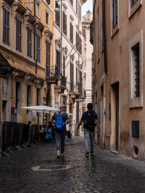 Free Tourists walking on a narrow cobblestone street in Rome, Italy, showcasing classic architecture. Stock Photo