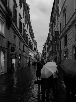 Rainy day in Rome's cobblestone street with pedestrians and umbrellas.