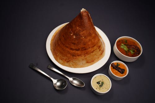 A plate with a large dosa and a bowl of food