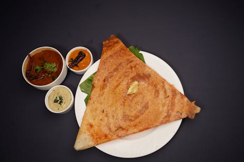 A white plate with a dosa and a bowl of sauce