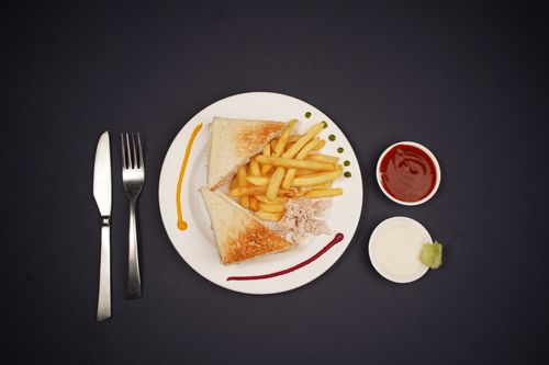 Free Top view of a sandwich with fries, condiments, and cutlery on a black background. Stock Photo