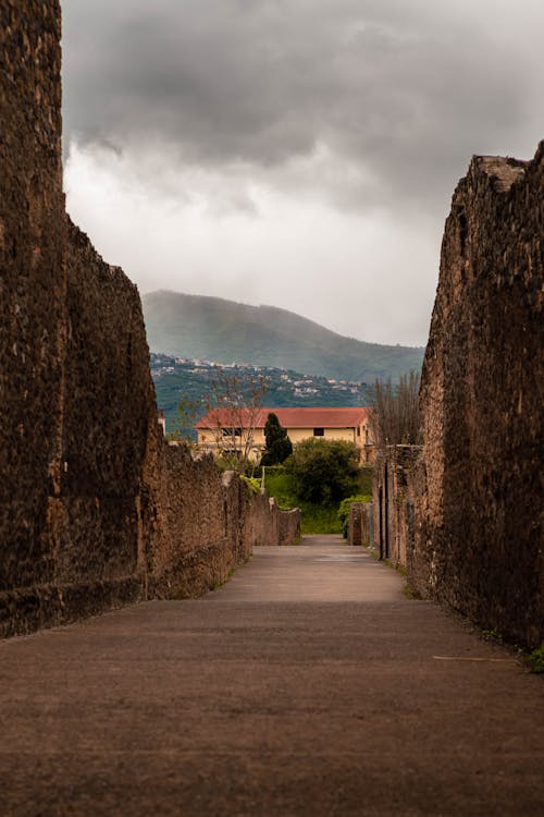 A narrow path leading to a building with a cloudy sky