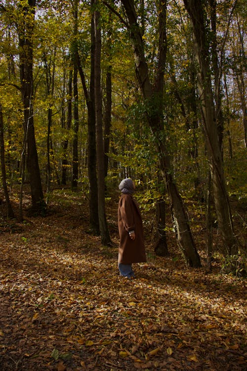 A woman in a brown coat walks through the woods