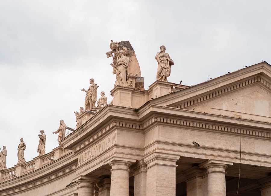Beautiful sculptures atop Vatican City's colonnades in daylight, showcasing classic artistry.