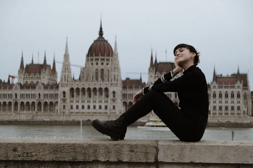 Young Woman Sitting on a Wall with the Hungarian Parliament Building in the Background 