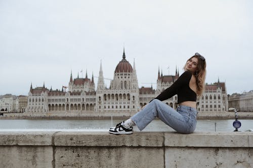 A woman sitting on a ledge in front of the budapest parliament building