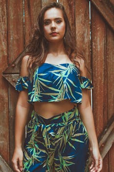 一位身着热带印花露肩上衣的女子在质朴的木制背景前摆着姿势