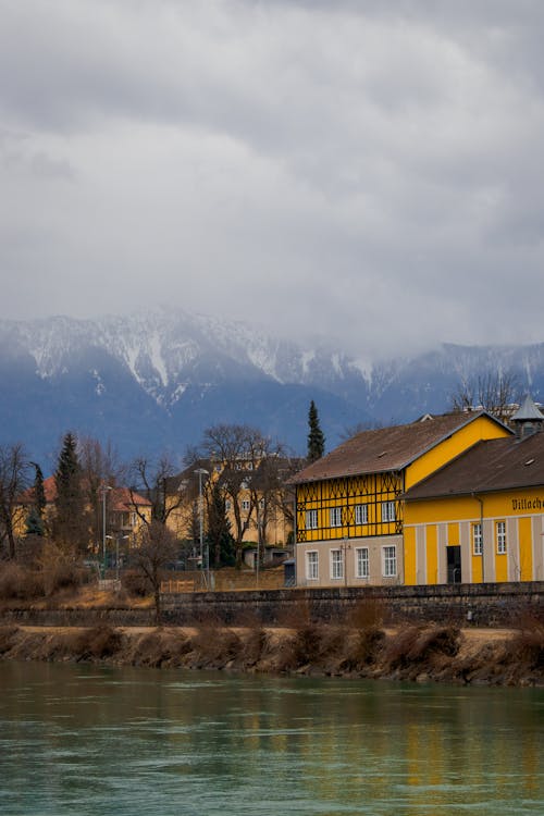 A yellow house sits next to a river and mountains