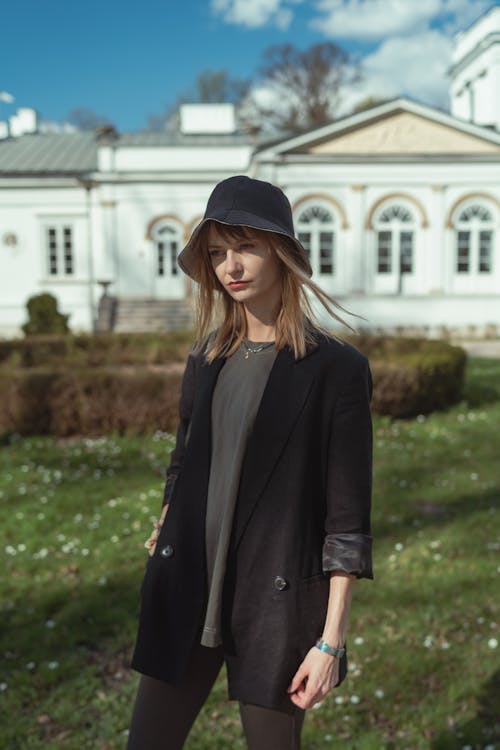 A woman in a black hat and jacket standing in front of a white building