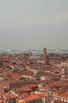 Aerial view showcasing Venice's historic architecture and iconic red rooftops under a cloudy sky.