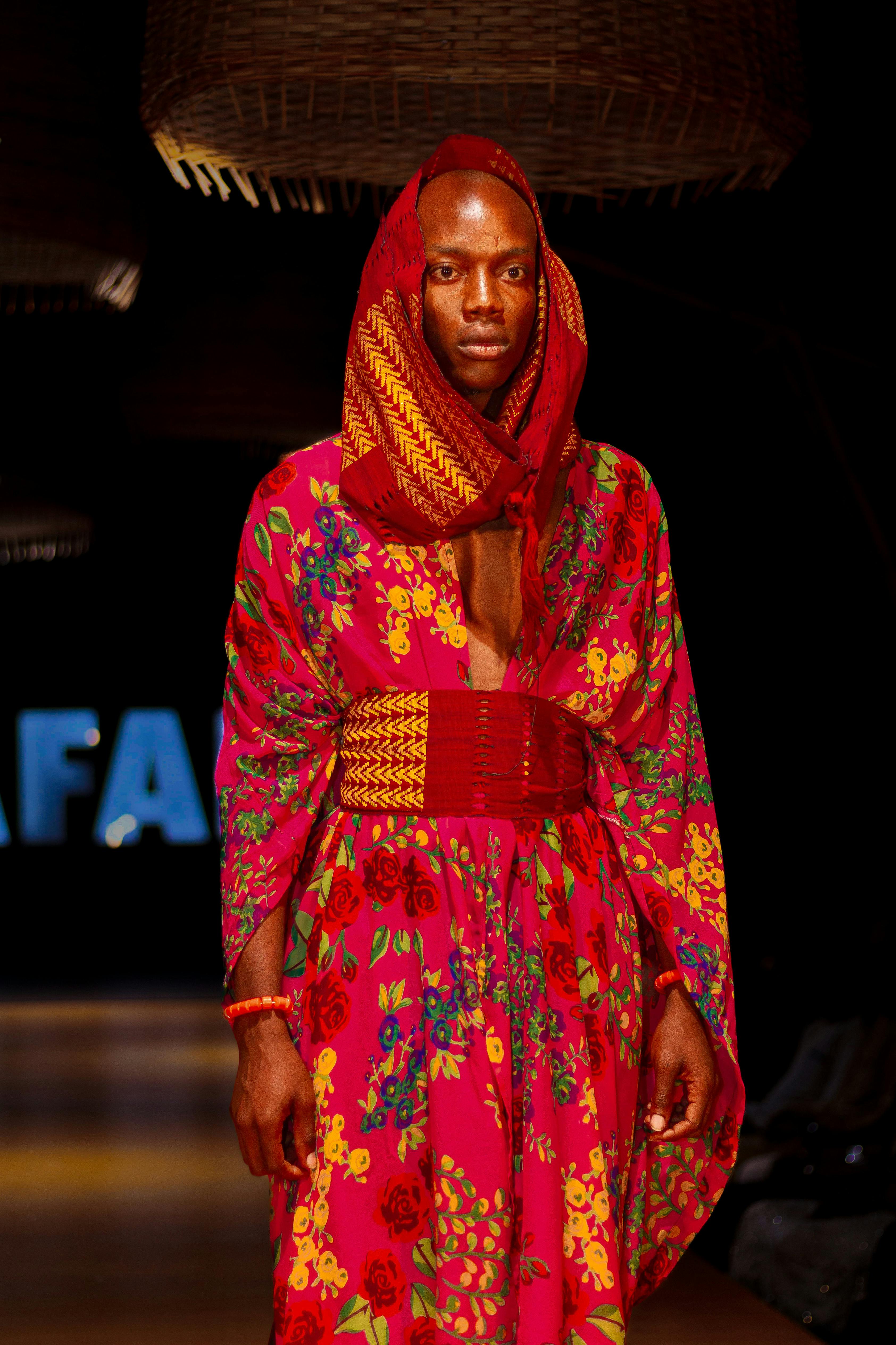A male model in colorful traditional clothing walks the runway at a fashion show.