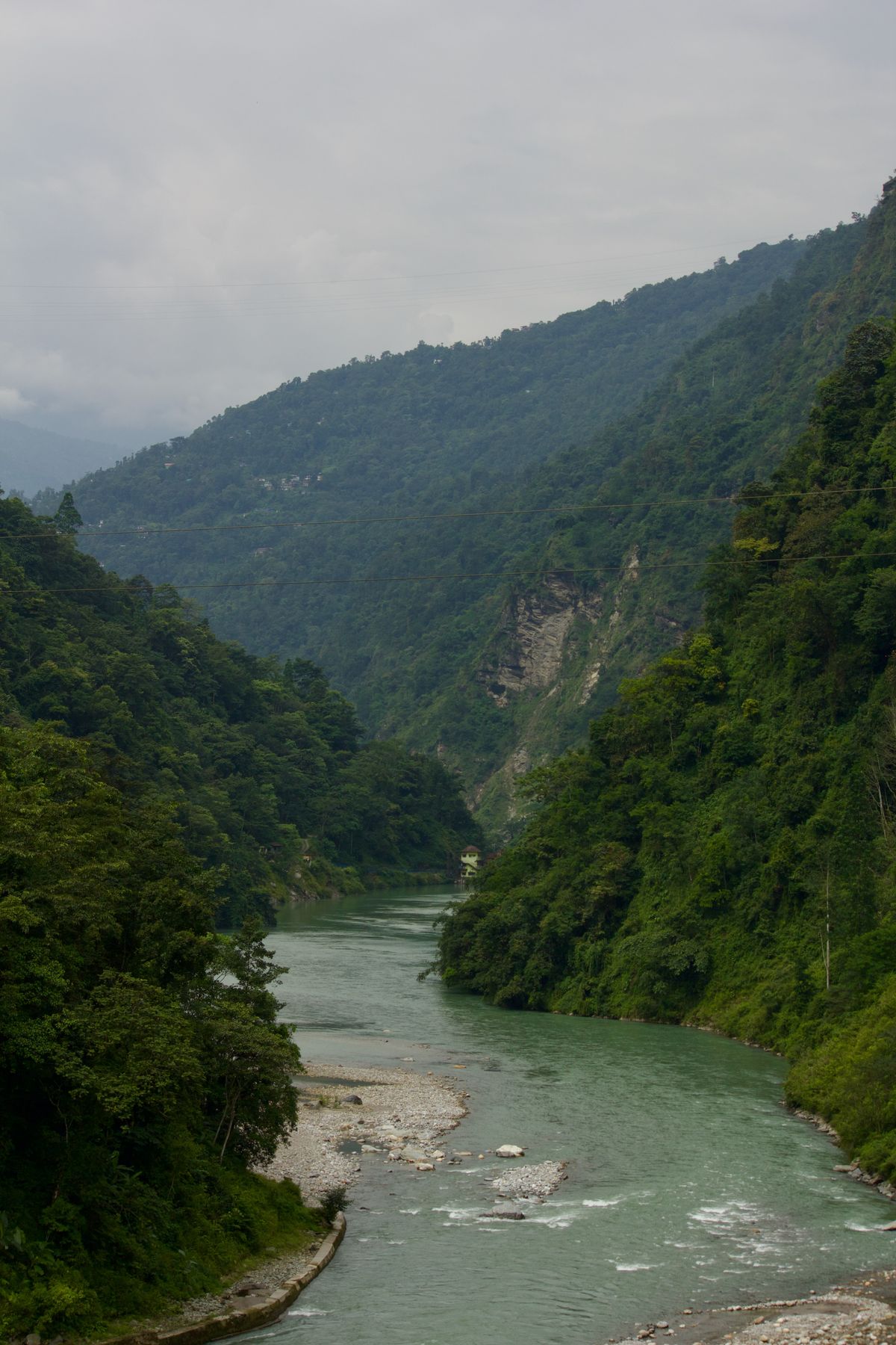 A jade green river running between steep forested slopes near Tashiding in West Sikkim, a shingle bank below