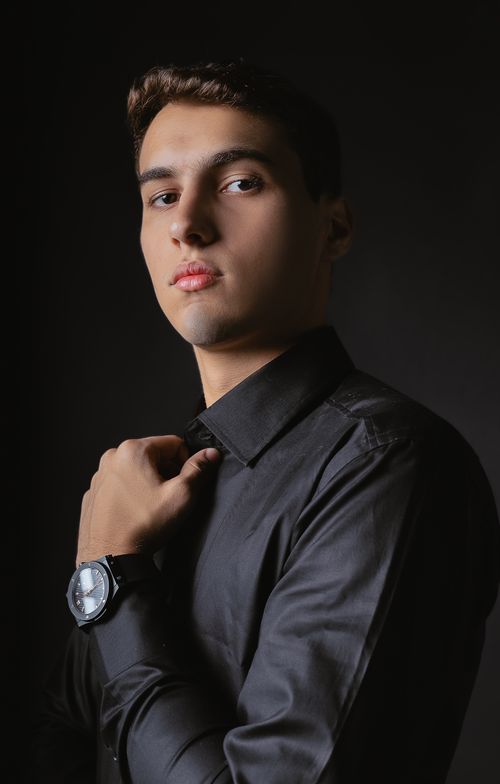 Free Sophisticated young man posing in black shirt, exuding elegance and style against a dark background. Stock Photo