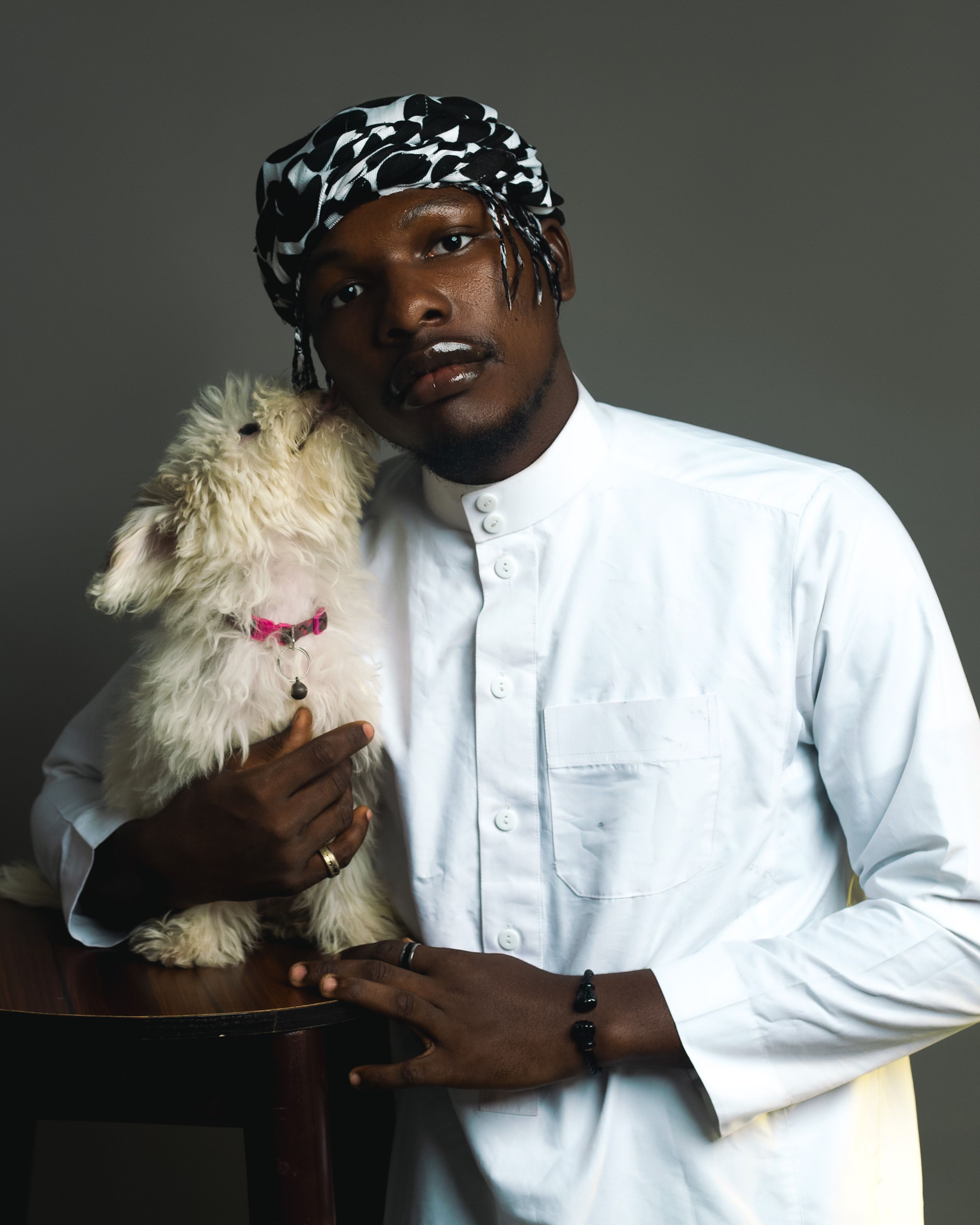 African man in traditional attire posing with fluffy dog indoors.
