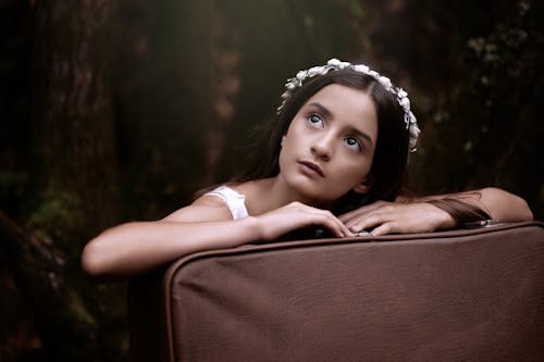 A young girl with a flower crown is sitting on a suitcase