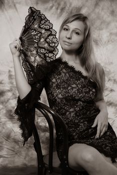 A woman elegantly poses in black lace with a hand fan in a monochrome studio setting.