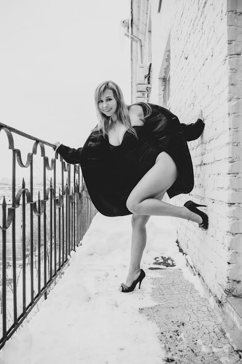  Smiling Woman in a Bodysuit and Coat Posing on a Balcony