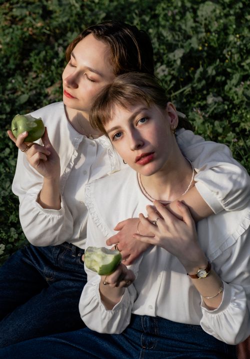 Free Two young women in white blouses enjoy green apples while sitting outside, embracing nature. Stock Photo