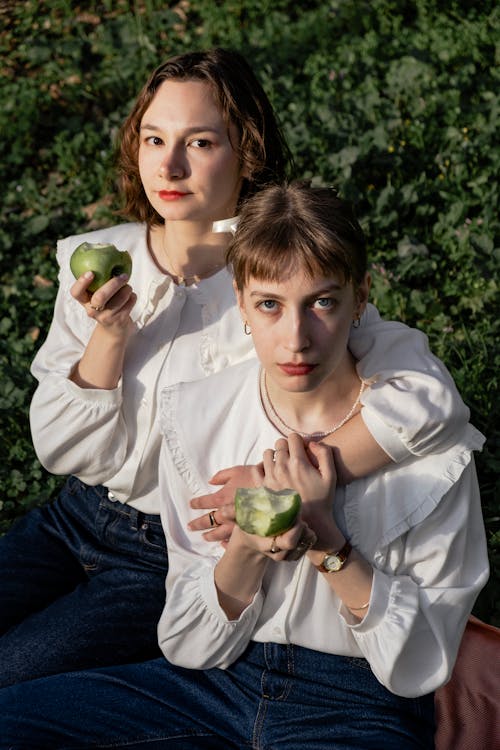 Two women in white shirts holding apples