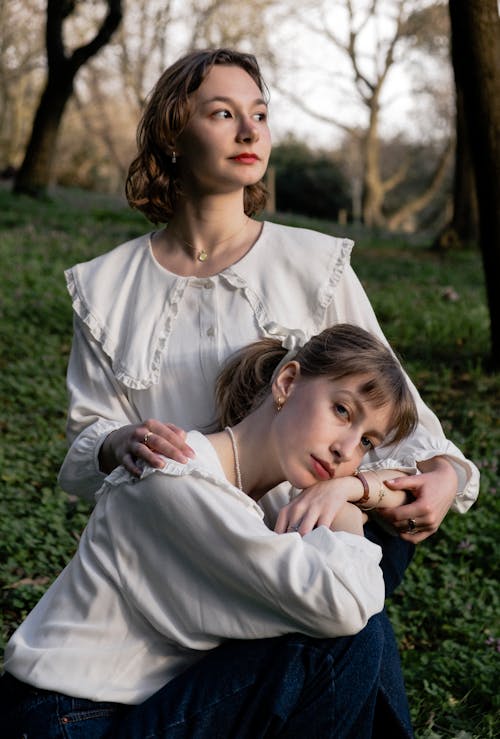 Two women sitting on the grass in front of a tree