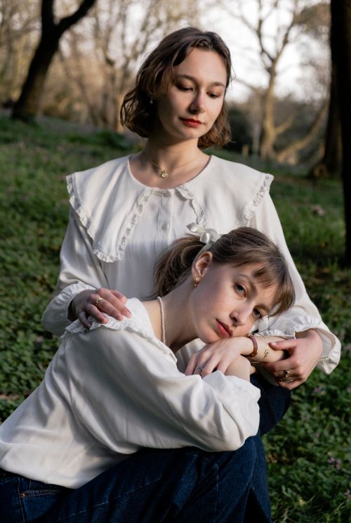 Free Two women wearing white blouses relax in a green park, showcasing serenity and togetherness. Stock Photo