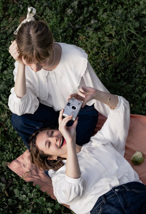 Two women are sitting on the grass taking pictures