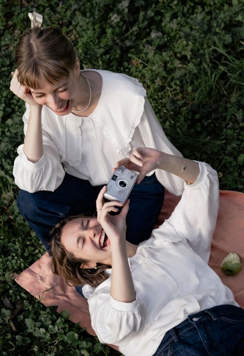 Free Two women enjoying a sunny day in the park, capturing joyful moments with a vintage camera. Stock Photo