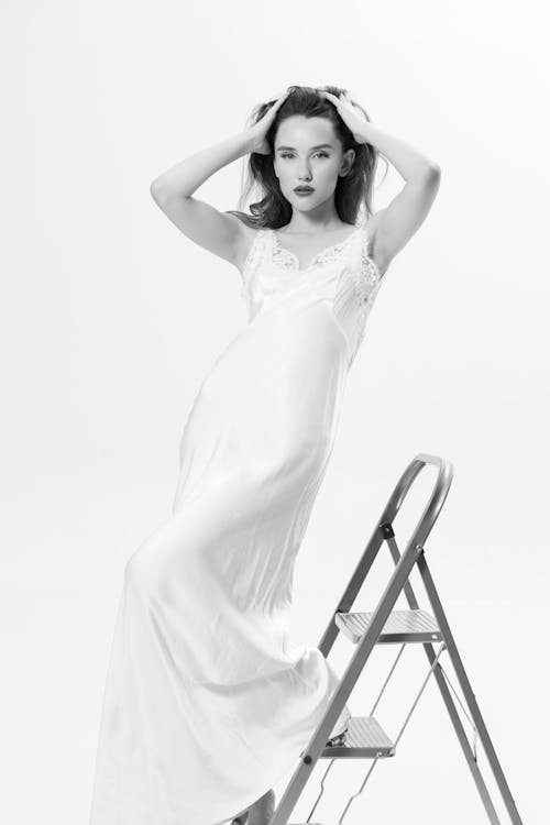 Studio Shot of a Woman in a Long Dress Standing next to a Ladder