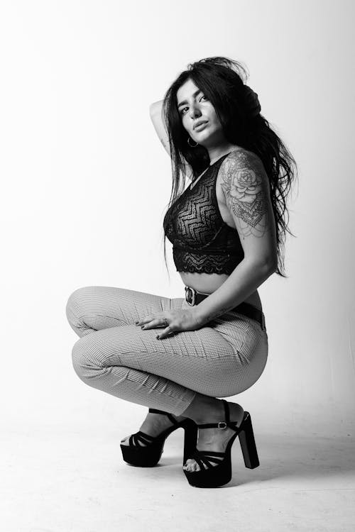 A woman in high heels squatting down in a black and white photo