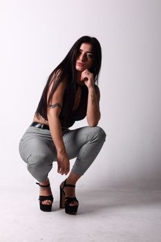 Stylish woman in high heels crouching on white background for a fashion photoshoot.