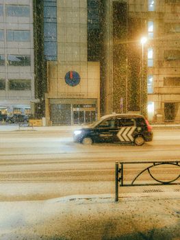 Taxi driving through a snowy city street at night, capturing urban winter atmosphere.