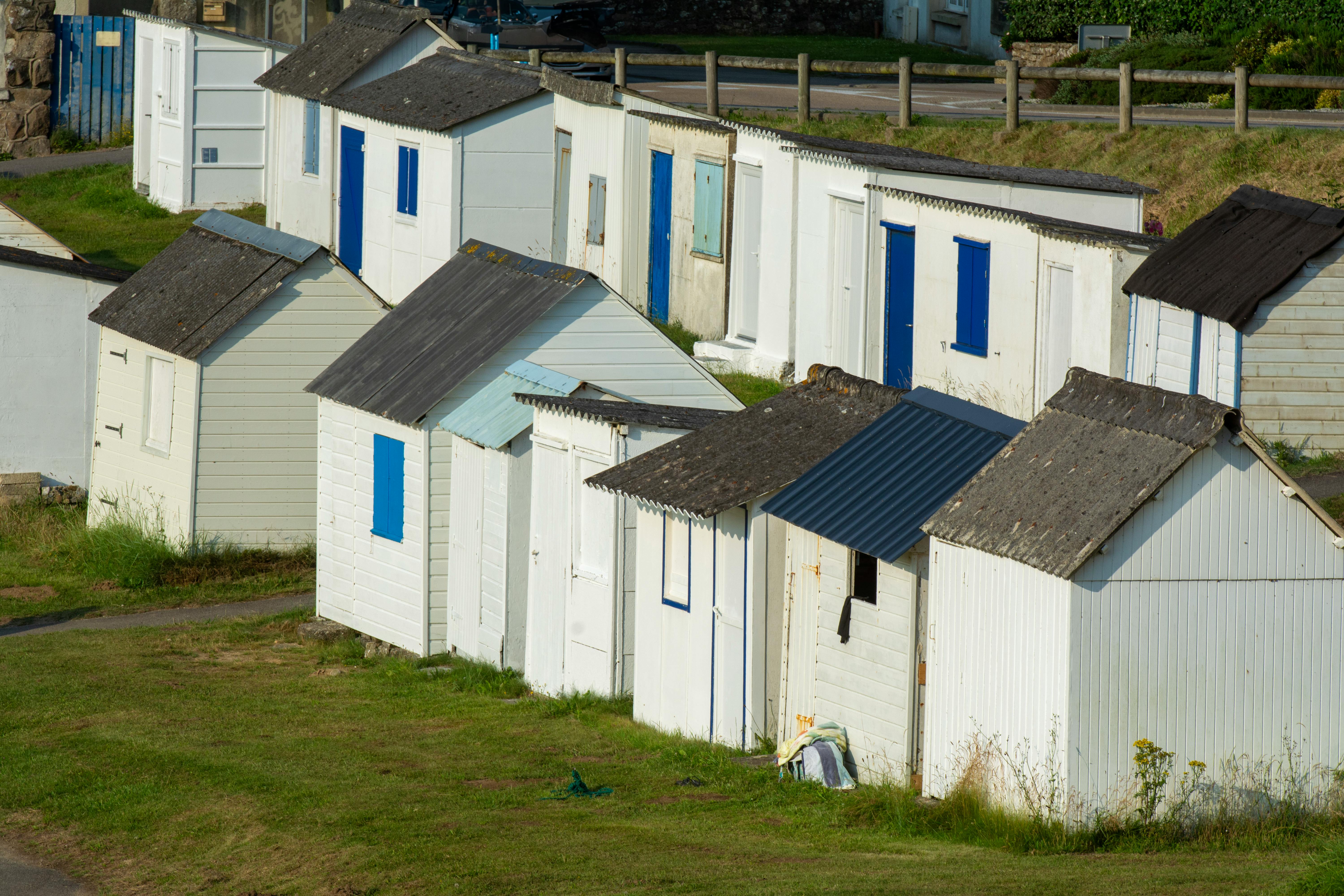 A row of charming white beach huts with blue accents in a serene rural environment.