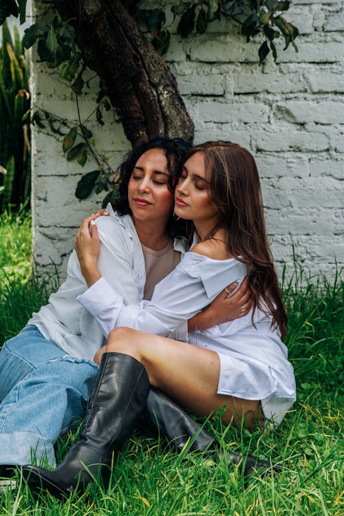 Two women sitting on the grass hugging each other