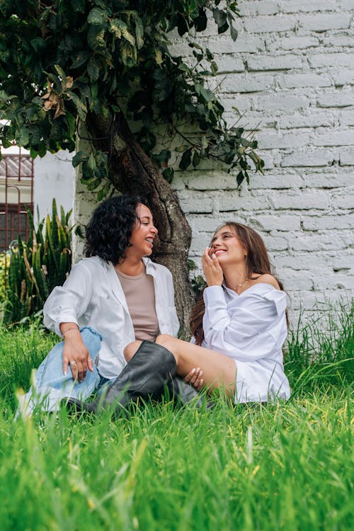 Two women sitting on the grass in front of a white building