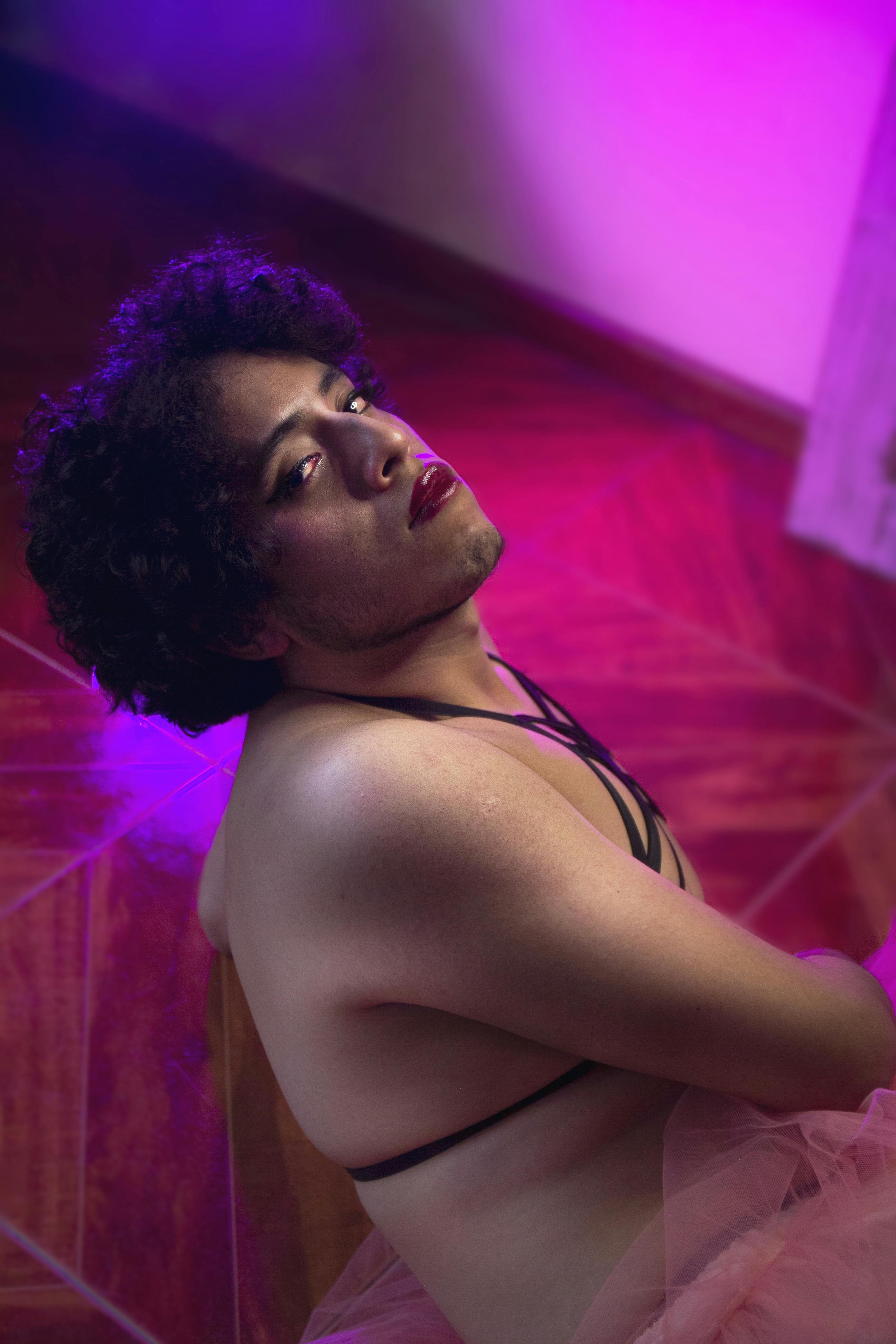 Free Portrait of a person sitting with dramatic pink lighting, highlighting fashion and expression. Stock Photo