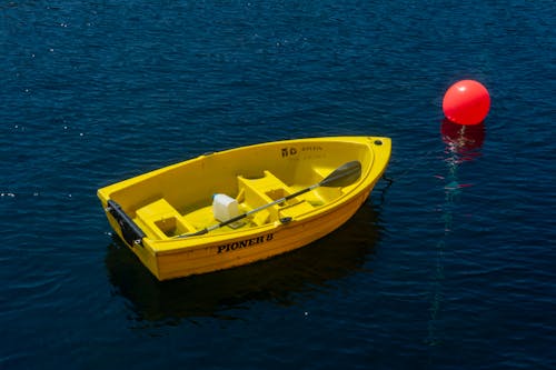 A yellow boat floating in the water with a red buoy