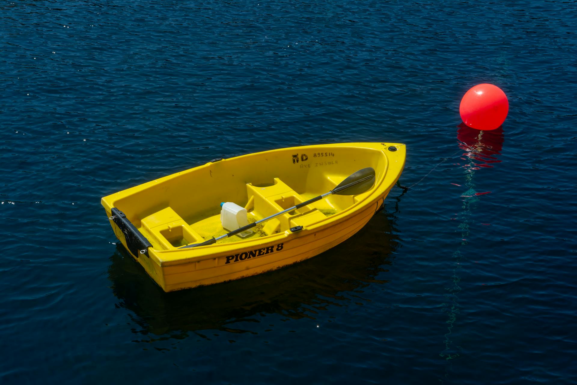 A bright yellow rowboat is tethered next to a red buoy on clear blue water, capturing a scene of calm leisure.