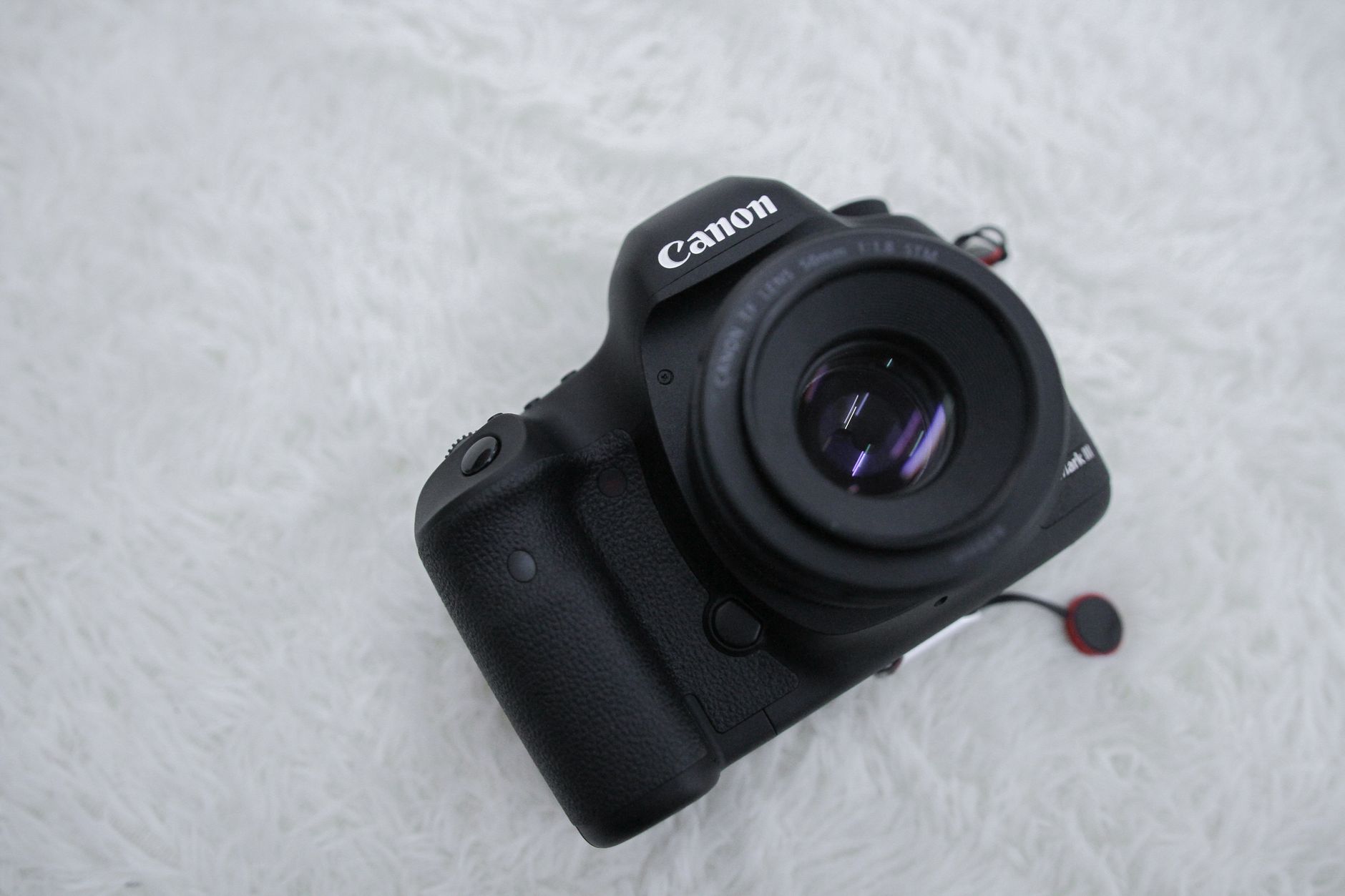 Canon DSLR camera featuring lens and design on a white fluffy surface, close-up shot.