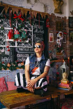 Person with sunglasses in a colorful cafe setting with eclectic decor and a blackboard menu.
